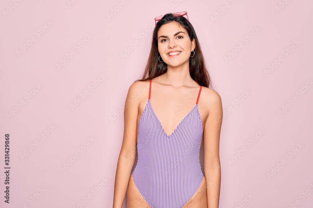 Young beautiful fashion girl wearing swimwear swimsuit and sunglasses over pink background with a happy and cool smile on face. Lucky person.