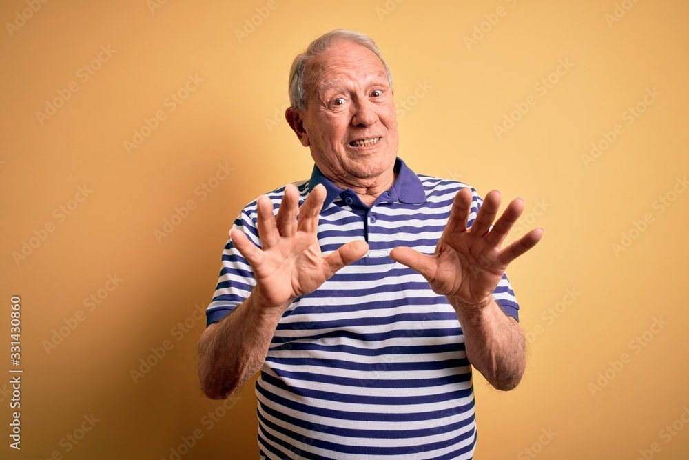 Grey haired senior man wearing casual navy striped t-shirt standing over yellow background afraid and terrified with fear expression stop gesture with hands, shouting in shock. Panic concept. Grey haired senior man wearing casual navy striped t-shirt standing over yellow background afraid and terrified with fear expression stop gesture with hands, shouting in shock. Panic concept.
