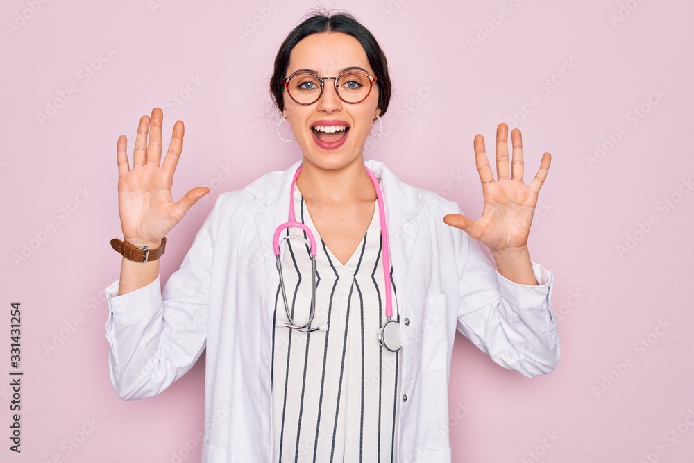 Beautiful doctor woman with blue eyes wearing coat and stethoscope over pink background showing and pointing up with fingers number ten while smiling confident and happy. Beautiful doctor woman with blue eyes wearing coat and stethoscope over pink background showing and pointing up with fingers number ten while smiling confident and happy.