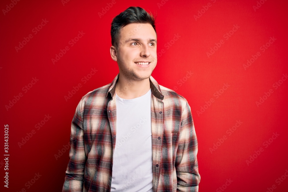 Young handsome caucasian man wearing casual modern shirt over red isolated background looking away to side with smile on face, natural expression. Laughing confident. Young handsome caucasian man wearing casual modern shirt over red isolated background looking away to side with smile on face, natural expression. Laughing confident.