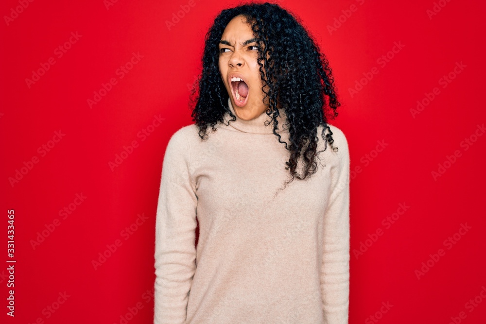 Young african american curly woman wearing casual turtleneck sweater over red background angry and mad screaming frustrated and furious, shouting with anger. Rage and aggressive concept. Young african american curly woman wearing casual turtleneck sweater over red background angry and mad screaming frustrated and furious, shouting with anger. Rage and aggressive concept.