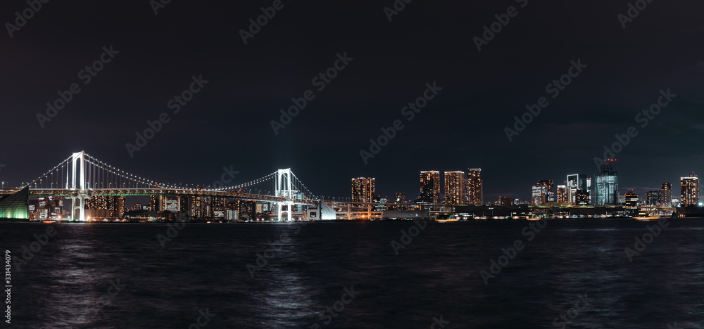 Night panorama of the Rainbow Bridge suspended over Tokyo Bay connecting the docks of Shibaura and the artificial island of Odaiba to Minato