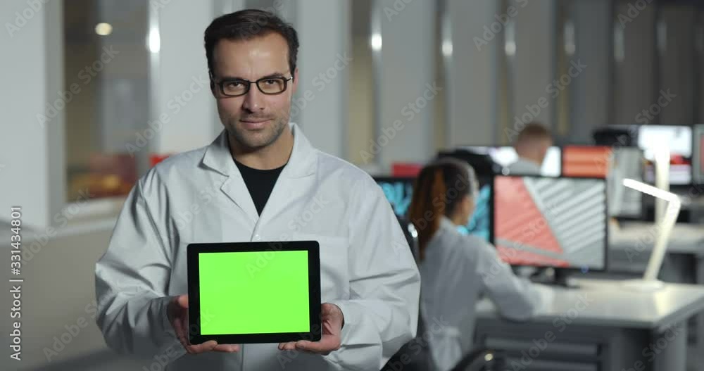 Smiling male engineer in lab coat showing green screen table Smiling male engineer in lab coat showing green screen table