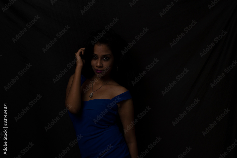 Fashion portrait of an young brunette Indian Bengali woman in vibrant blue western dress in dark studio copy space background. Indian lifestyle and fashion.