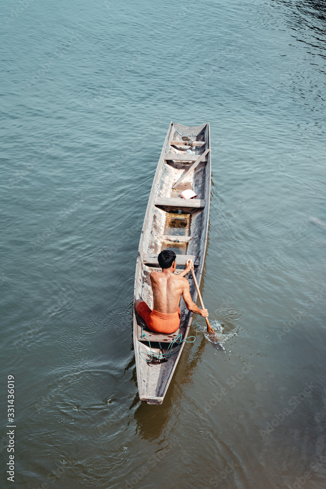 A resident of Laos paddling aboard a traditional boat on the Mekong