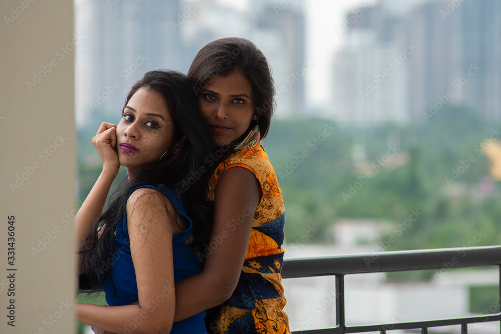 Portrait of two young and beautiful brunette Bengali woman in western dress standing on a balcony and enjoying themselves in green urban background. Indian lifestyle. Portrait of two young and beautiful brunette Bengali woman in western dress standing on a balcony and enjoying themselves in green urban background. Indian lifestyle.