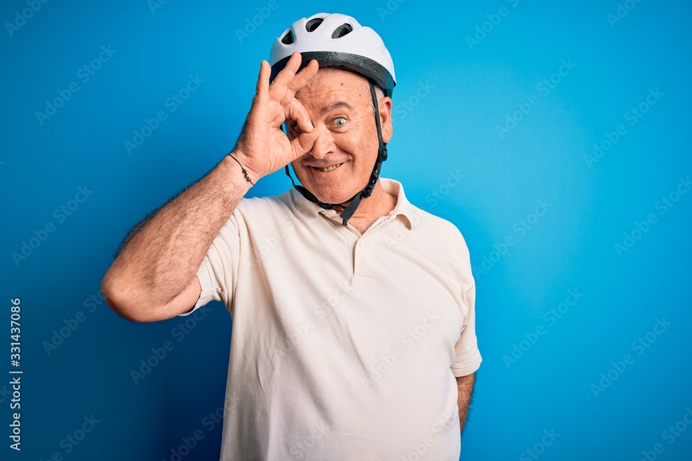 Middle age hoary cyclist man wearing bike security helmet over isolated blue background doing ok gesture with hand smiling, eye looking through fingers with happy face. Middle age hoary cyclist man wearing bike security helmet over isolated blue background doing ok gesture with hand smiling, eye looking through fingers with happy face.