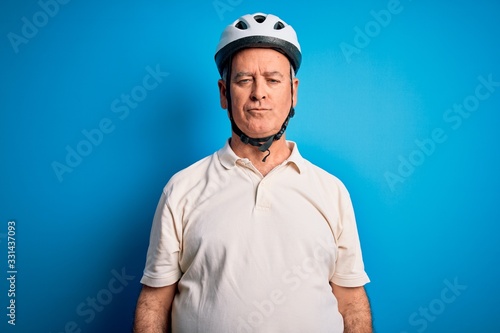 Middle age hoary cyclist man wearing bike security helmet over isolated blue background with serious expression on face. Simple and natural looking at the camera.