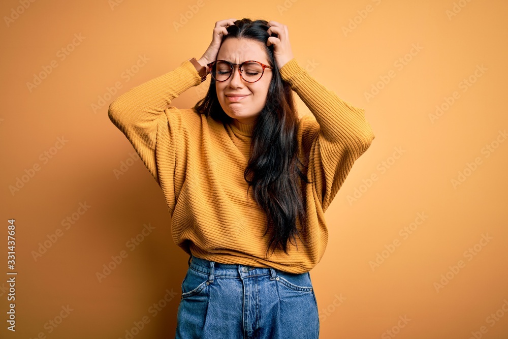 Young brunette woman wearing glasses and casual sweater over yellow isolated background suffering from headache desperate and stressed because pain and migraine. Hands on head. Young brunette woman wearing glasses and casual sweater over yellow isolated background suffering from headache desperate and stressed because pain and migraine. Hands on head.
