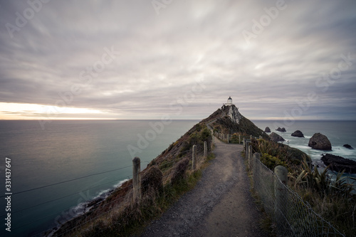 Gorgeous pink sunrise panorama at Nugget Point Lighthouse taken on a cloudy winter day, New Zealand