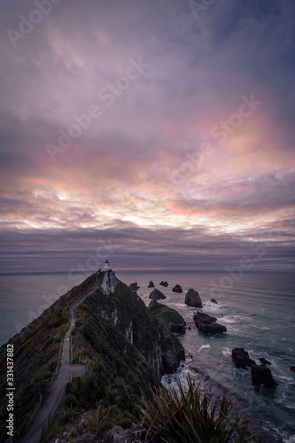 Gorgeous pink sunrise panorama at Nugget Point Lighthouse taken on a cloudy winter day, New Zealand