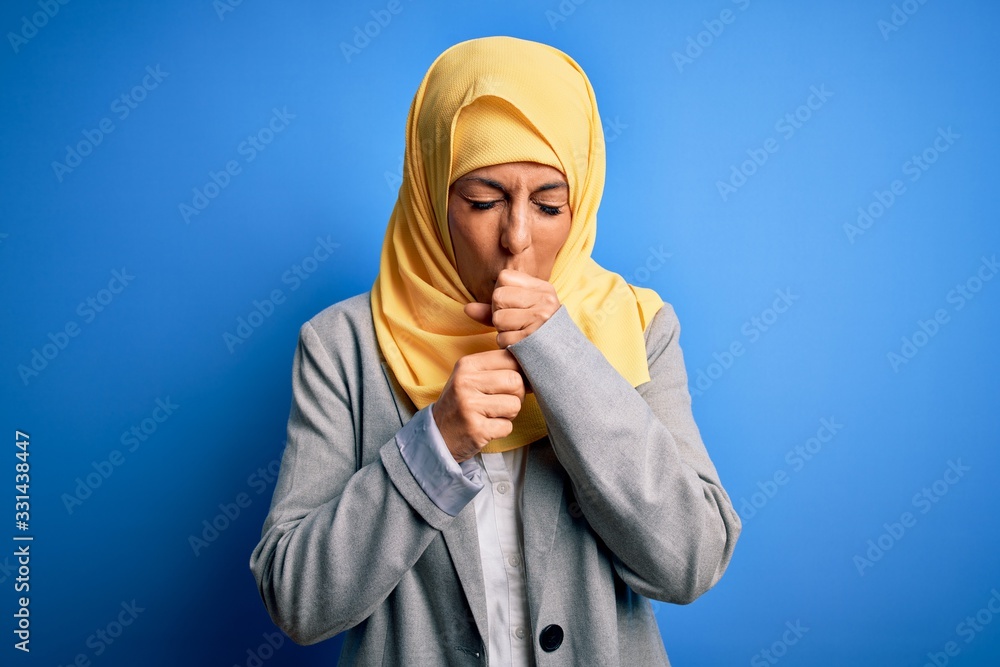 Middle age brunette business woman wearing muslim traditional hijab over blue background feeling unwell and coughing as symptom for cold or bronchitis. Health care concept. Middle age brunette business woman wearing muslim traditional hijab over blue background feeling unwell and coughing as symptom for cold or bronchitis. Health care concept.
