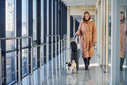 Young female passenger in warm clothes walking with her dog in airport hall