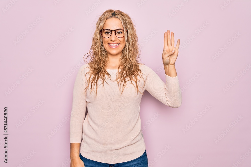 Young beautiful blonde woman wearing casual sweater and glasses over pink background showing and pointing up with fingers number four while smiling confident and happy. Young beautiful blonde woman wearing casual sweater and glasses over pink background showing and pointing up with fingers number four while smiling confident and happy.
