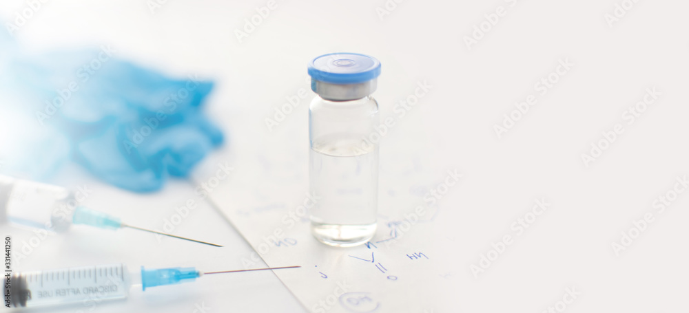 Banner with medicine bottle, blue rubber gloves, syringes and paper with handwritten chemical formulas on light background. Coronavirus vaccine development. 2019-nCoV liquid drug, antidote. Copy space Banner with medicine bottle, blue rubber gloves, syringes and paper with handwritten chemical formulas on light background. Coronavirus vaccine development. 2019-nCoV liquid drug, antidote. Copy space