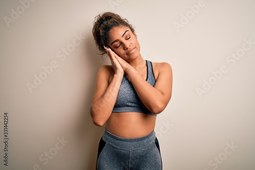 Young african american sportswoman doing sport wearing sportswear over white background sleeping tired dreaming and posing with hands together while smiling with closed eyes.