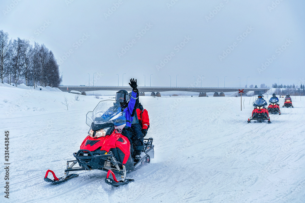 People on snowmobile waving hand at frozen lake winter Rovaniemi
