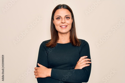 Young beautiful brunette woman wearing casual t-shirt standing over isolated white background happy face smiling with crossed arms looking at the camera. Positive person.