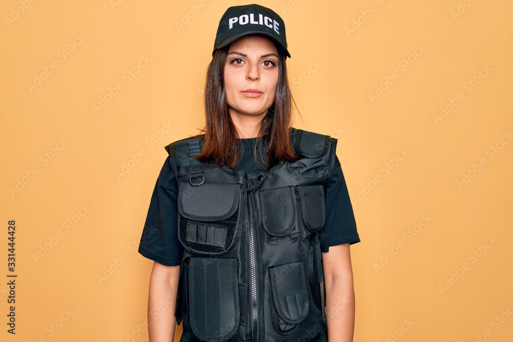 Young beautiful brunette policewoman wearing police uniform bulletproof and cap Relaxed with serious expression on face. Simple and natural looking at the camera. Young beautiful brunette policewoman wearing police uniform bulletproof and cap Relaxed with serious expression on face. Simple and natural looking at the camera.