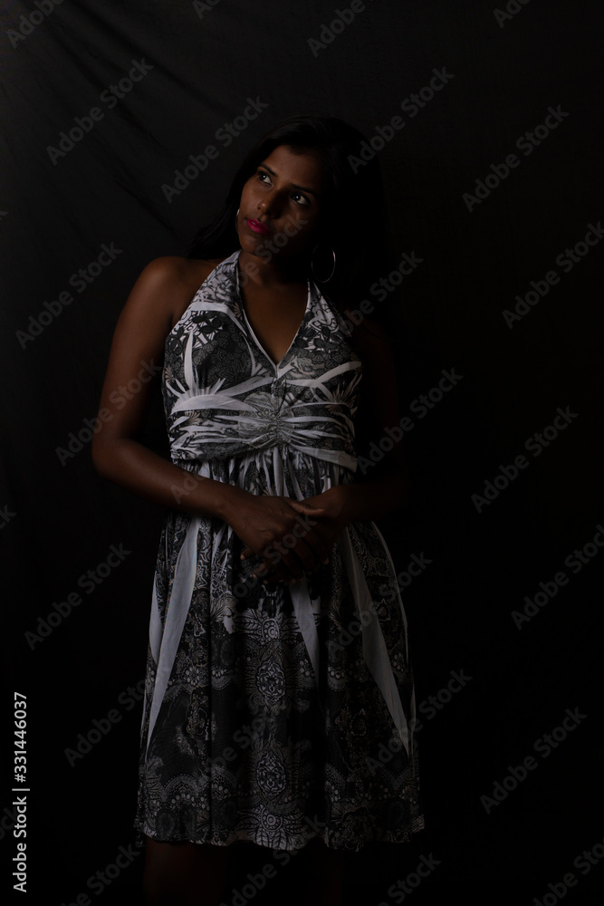 Fashion portrait of a dark skinned young brunette Indian Bengali woman in white western dress in dark studio copy space background. Indian lifestyle and fashion.