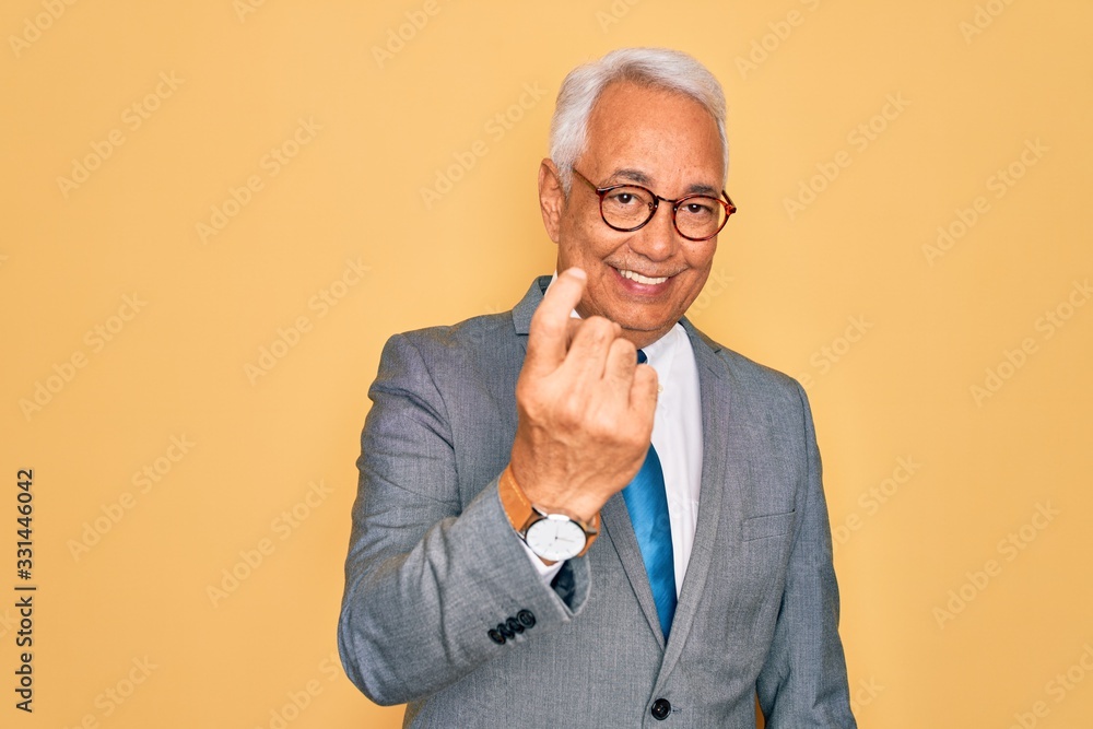 Middle age senior grey-haired handsome business man wearing glasses over yellow background Beckoning come here gesture with hand inviting welcoming happy and smiling Middle age senior grey-haired handsome business man wearing glasses over yellow background Beckoning come here gesture with hand inviting welcoming happy and smiling