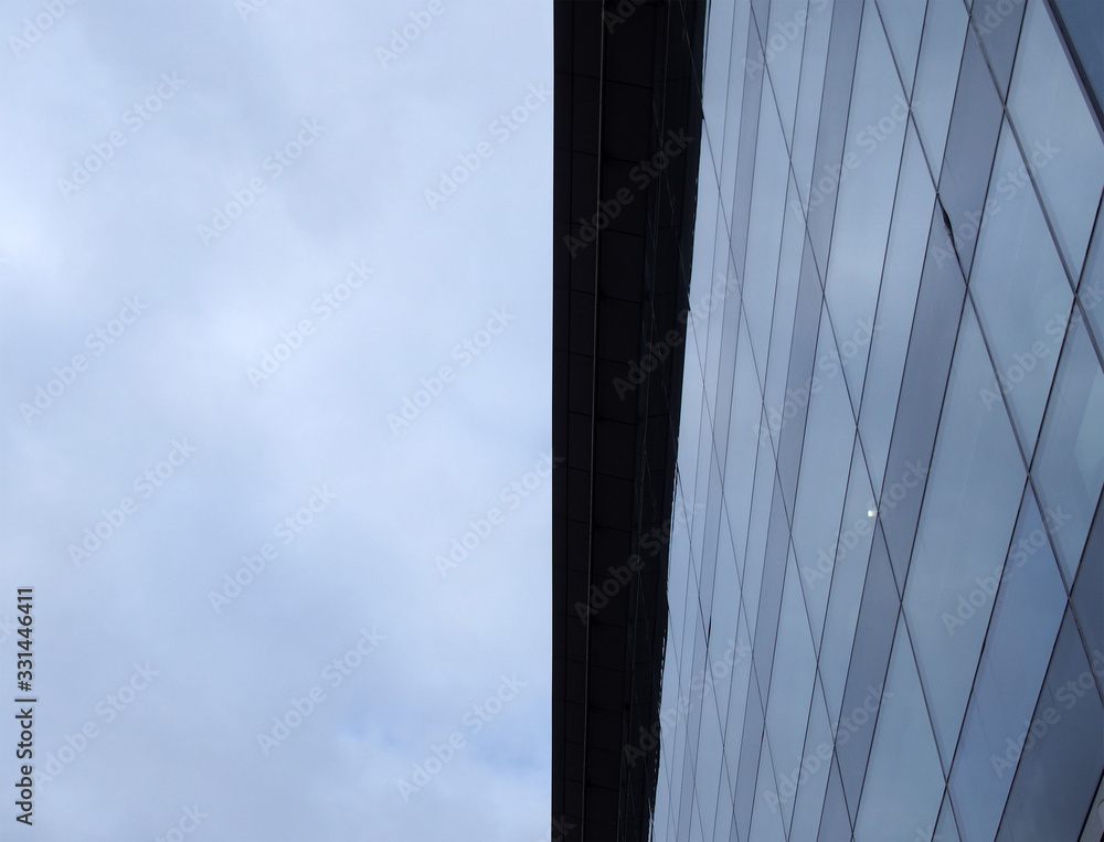 vertical upwards view of a modem office building with a blue cloudy sky on one side reflected in the windows vertical upwards view of a modem office building with a blue cloudy sky on one side reflected in the windows
