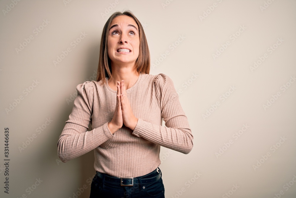 Young beautiful woman wearing casual sweater standing over isolated white background begging and praying with hands together with hope expression on face very emotional and worried. Begging. Young beautiful woman wearing casual sweater standing over isolated white background begging and praying with hands together with hope expression on face very emotional and worried. Begging.