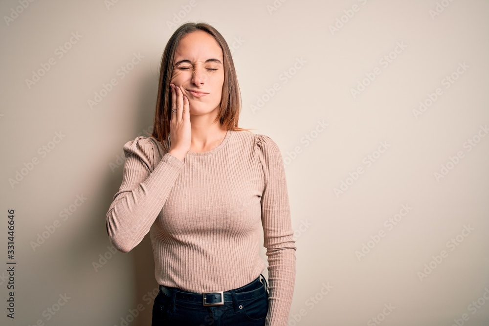 Young beautiful woman wearing casual sweater standing over isolated white background touching mouth with hand with painful expression because of toothache or dental illness on teeth. Dentist Young beautiful woman wearing casual sweater standing over isolated white background touching mouth with hand with painful expression because of toothache or dental illness on teeth. Dentist