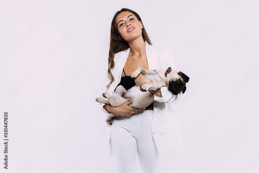 A laughing and smiling auburn haired woman in a white dress, is staring most lovingly at her cute pug, who calmly sits on the hands, gaining her undivided attention. Isolated white background. A laughing and smiling auburn haired woman in a white dress, is staring most lovingly at her cute pug, who calmly sits on the hands, gaining her undivided attention. Isolated white background.