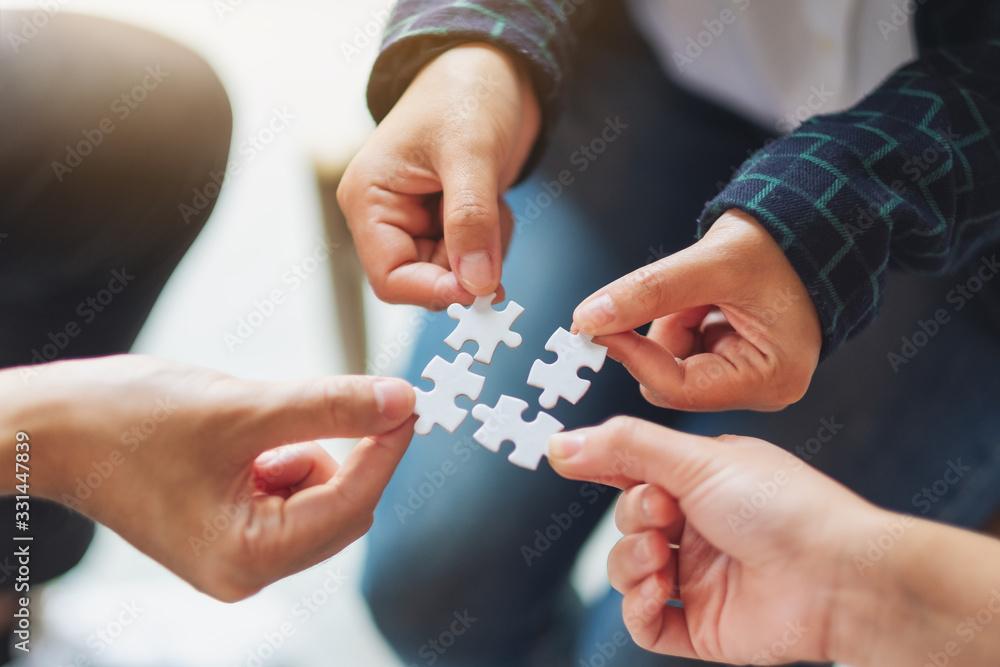 Closeup image of a group of people holding and putting a piece of white jigsaw puzzle together