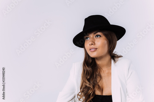 A laughing and smiling auburn haired woman in a white dress and black hat. Sittion on the wooden pallet. Isolated white background.