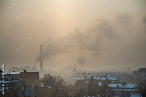 Cold winter day in the city. There is a smoking chimney on the horizon. The sun is shining through the polluted air.