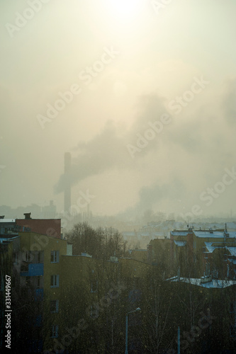 Cold winter day in the city. There is a smoking chimney on the horizon. The sun is shining through the polluted air.