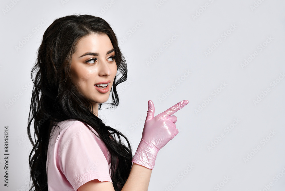 Girl in pink uniform and disposable gloves standing sideways, isolated on white. She smiling, pointing at something. Close up Girl in pink uniform and disposable gloves standing sideways, isolated on white. She smiling, pointing at something. Close up