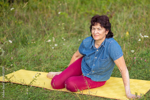 Beautiful mature women sits in Zelenaya Polyana on the mat after gymnastics on a summer day. photo