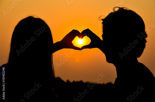 Silhouette of the young couple make a heart shape with their hands during a romantic holiday