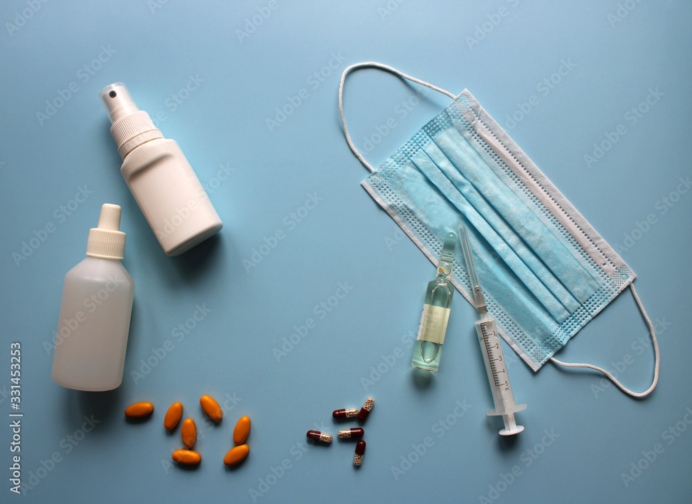 Naklejka premium Medical mask with ampoule, syringe, antiseptic, medicines on a blue background. Covid19, coronavirus and epidemic content. Virus prevention and creating a vaccine against coronavirus. Copy space