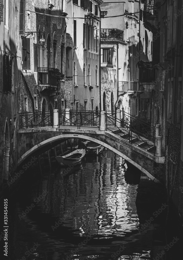Streets of Venice in black and white monochrome with traditional houses and a bridge reflecting on the waterway of the city 