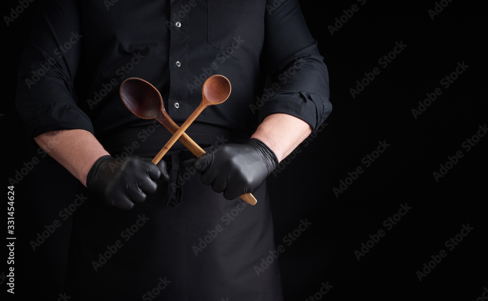 chef in black latex gloves and a black uniform holds crossed wooden vintage spoons