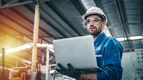 Confident engineer in blue jumpsuit holding laptop computer in a warehouse. photo