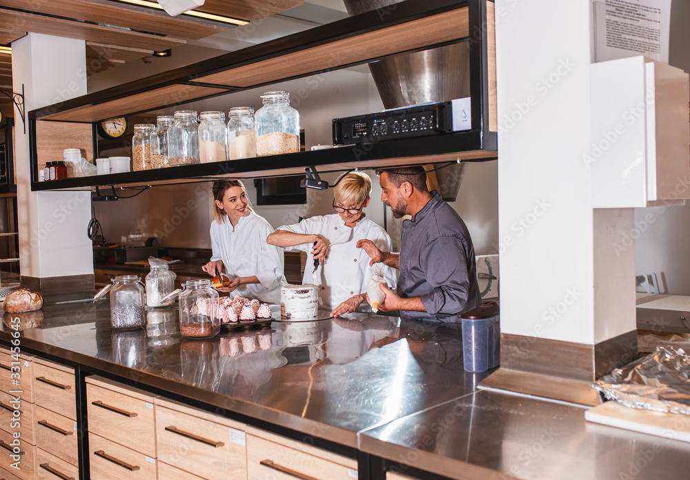 Group of workers in uniform decorating desserts in modern manufacturing. Group of workers in uniform decorating desserts in modern manufacturing.