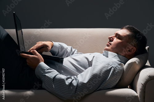 businessman is lying on the sofa and working with laptop