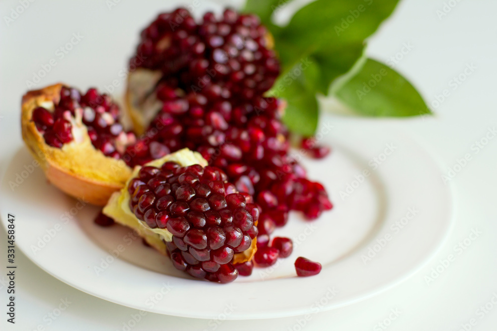 Juicy opened pomegranate with leaves on a white background. Eco healthy food. Grains of natural pomegranate. Juicy opened pomegranate with leaves on a white background. Eco healthy food. Grains of natural pomegranate.