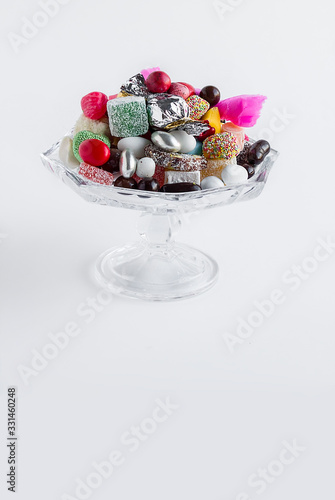 Traditional,colorful candies "almond,akide,delight"and chocolates in glass candy bowl,on white with copy space.