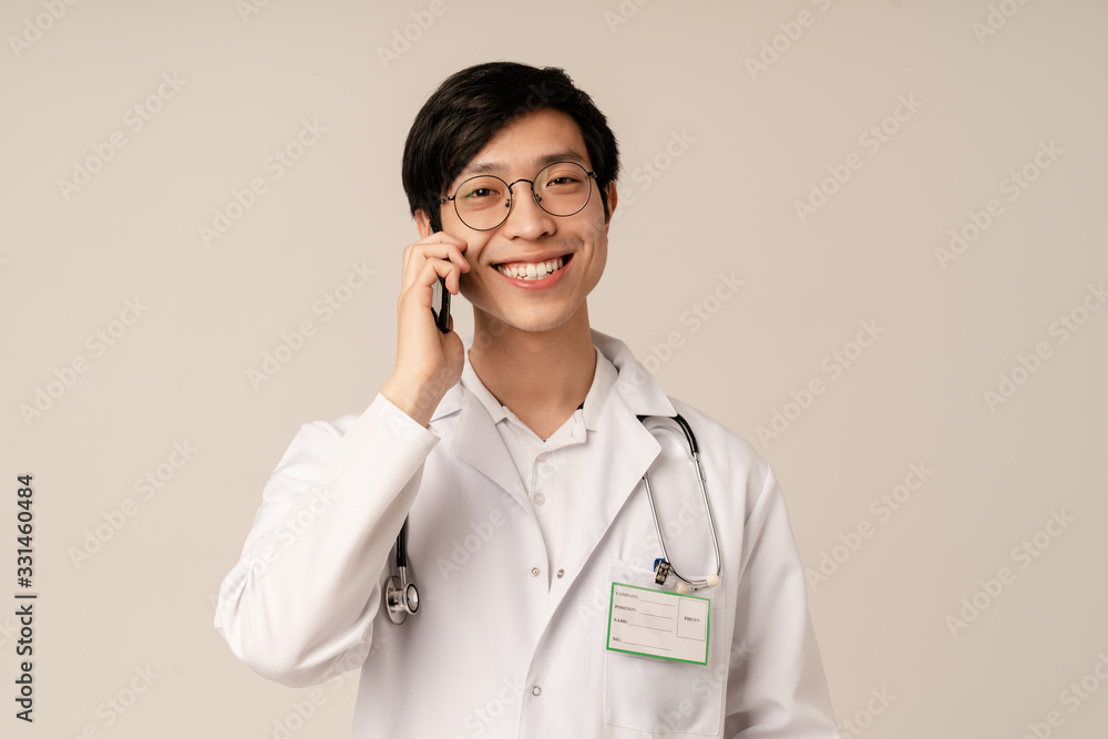 Image of asian young doctor in uniform smiling and talking on cellphone Image of asian young doctor in uniform smiling and talking on cellphone