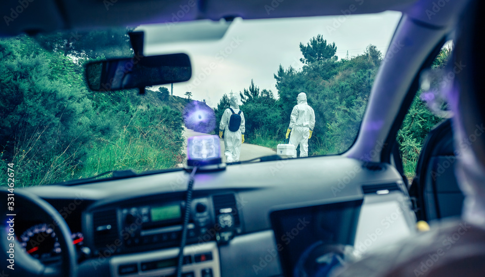 View from inside the car of people in bacteriological protection suits doing research on an empty road
