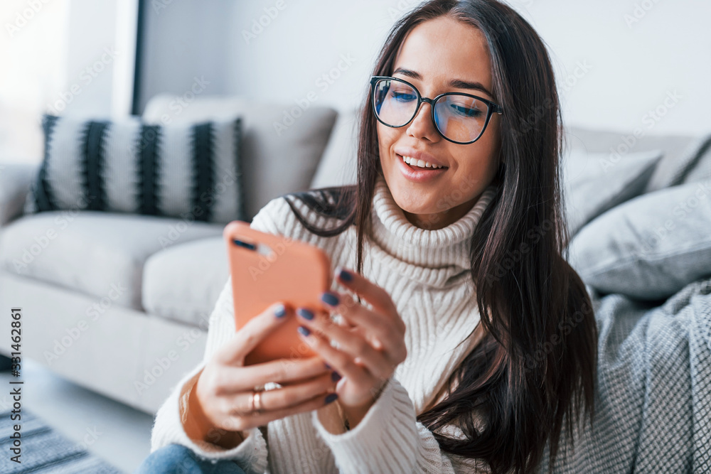 Young beautiful woman in glasses sitting at home alone with phone in hands Young beautiful woman in glasses sitting at home alone with phone in hands