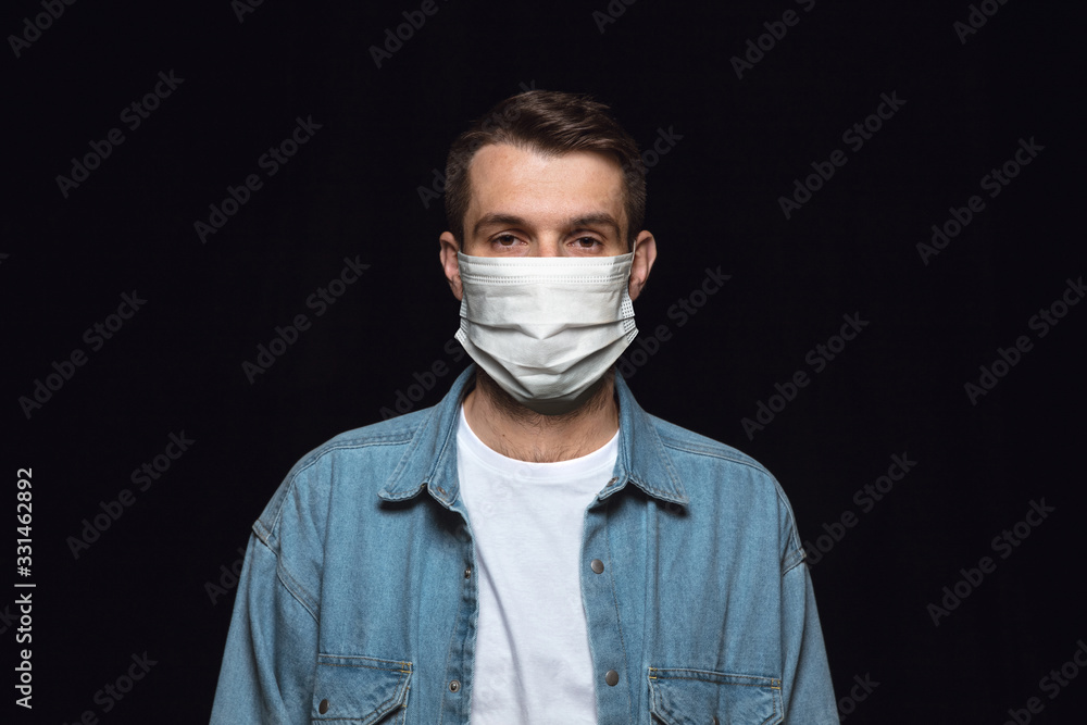 Serious man in protective mask on black background. Prevention against pneumonia, keep on being on quarantine, staying home. Chinese coronavirus treatment. Healthcare, medicine, isolation concept. Serious man in protective mask on black background. Prevention against pneumonia, keep on being on quarantine, staying home. Chinese coronavirus treatment. Healthcare, medicine, isolation concept.