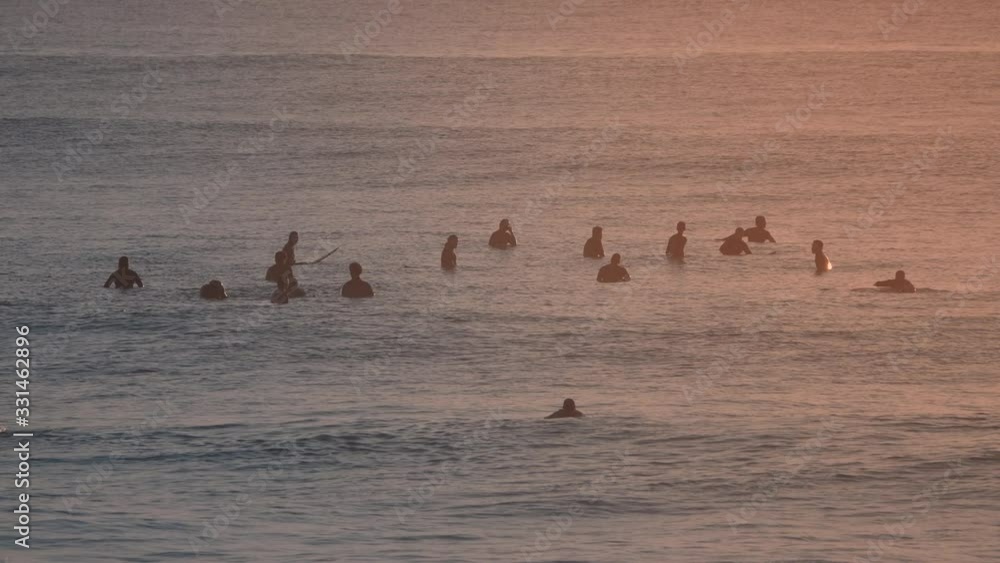 Steady shot of a bunch of surfers waiting for a perfect wave. Extreme sport at the sunset/sunrise. Steady shot of a bunch of surfers waiting for a perfect wave. Extreme sport at the sunset/sunrise.