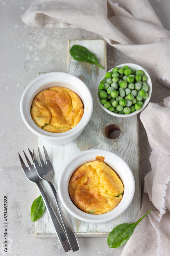 Green peas and cheese souffle in a white ceramic ramekin on light wooden board. Classic french meal. Top view.